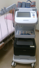 キャスター付きの機械で、モニターや4つのカフなどがついている血圧脈波測定装置の写真